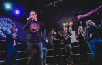 Sam West speaks to a Wrestling Resurgence audience from inside the wrestling ring as performers and collaborators applaud.